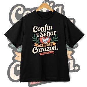 May include: Black t-shirt with a graphic design featuring the words "Conf&iacute;a en el Se&ntilde;or con todo tu coraz&oacute;n" in white and cream lettering, a red heart, and a white dove. The text "Proverbios 3:5" is also included.