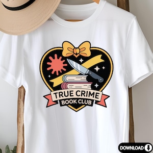 May include: White t-shirt featuring a graphic design with a black heart, a knife, books, and the text "TRUE CRIME BOOK CLUB". The design includes a yellow bow and a red sunburst.