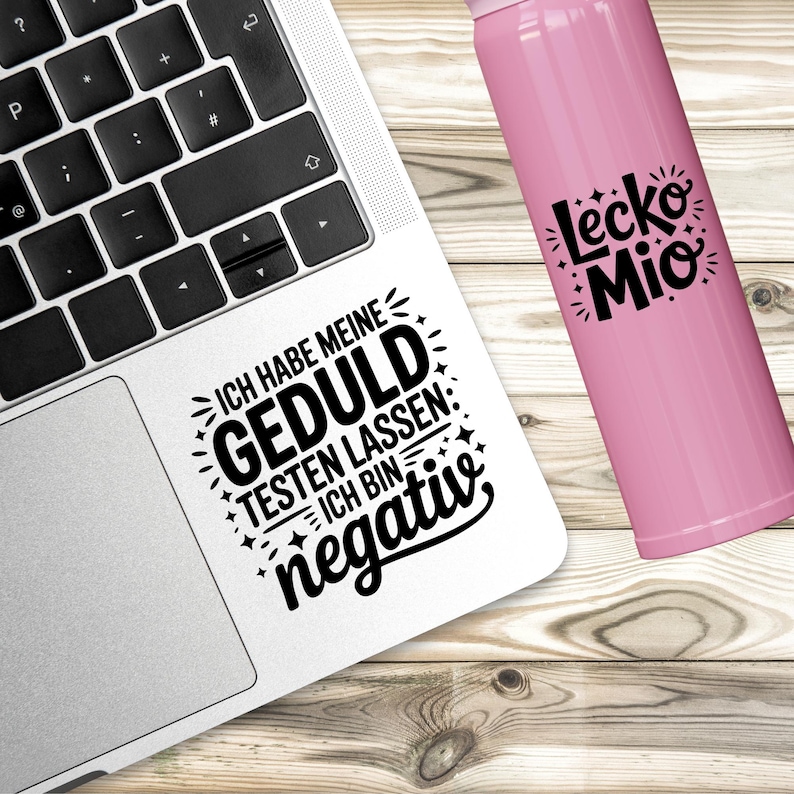 Puede incluir: Un port&aacute;til blanco con una pegatina que dice "ICH HABE MEINE GEDULD TESTEN LASSEN: ICH BIN negativ" en negro. Una botella de agua rosa con el texto "Lecko Mio" est&aacute; al lado.