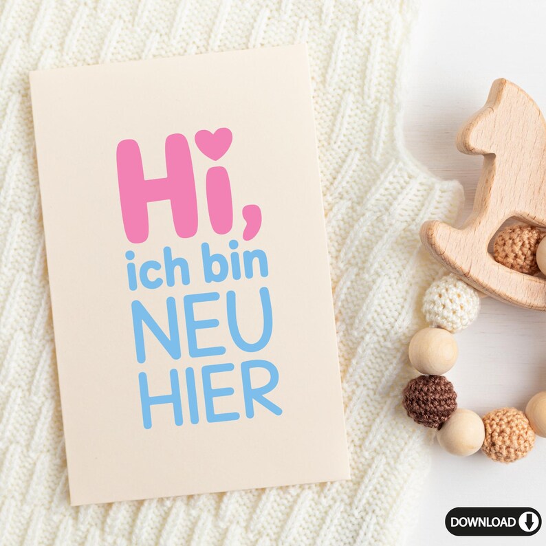 May include: A light beige card with the text "Hi, ich bin NEU HIER" in pink and blue. A wooden horse toy and a beaded teething ring are next to the card on a white knitted blanket.