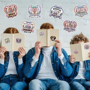 May include: Three people holding open books with stickers on them, in front of their faces. Above them are heart-shaped stickers with text that reads "Spicy Book Club", "Second Chance Love Book Club", "Magical Book Club", "Fairy Tale Retelling Book Club", "Romance Book Club", and "Gothic Tales Book Club".
