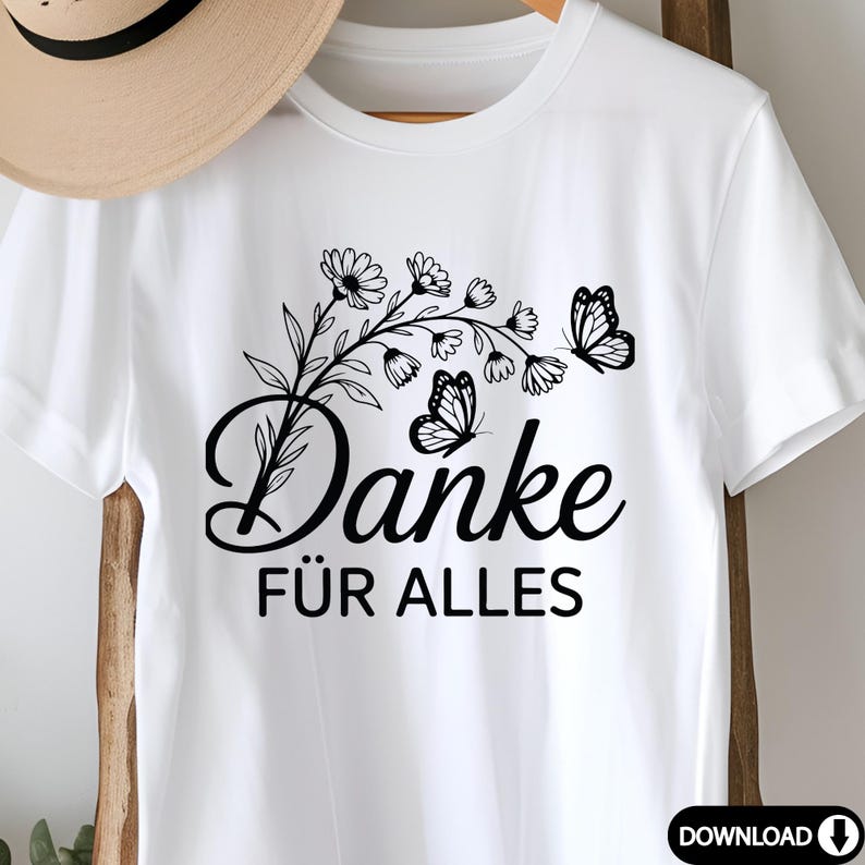 May include: White t-shirt with a black floral and butterfly design and the German words "Danke F&uuml;r Alles". The design includes a floral branch with daisies and two butterflies.