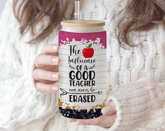 May include: A pink and black tumbler with a bamboo lid and a straw. The tumbler has a white background with black lines and the text "The Influence of a Good Teacher can never be Erased". There is a red apple with a leaf on the tumbler.