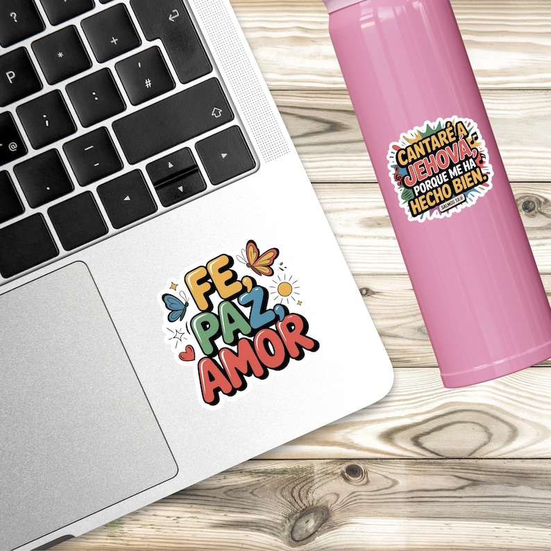 May include: A white sticker with the words "FE, PAZ, AMOR" in colorful bubble letters, with butterfly and sun illustrations. A pink water bottle and a laptop are also in the image.