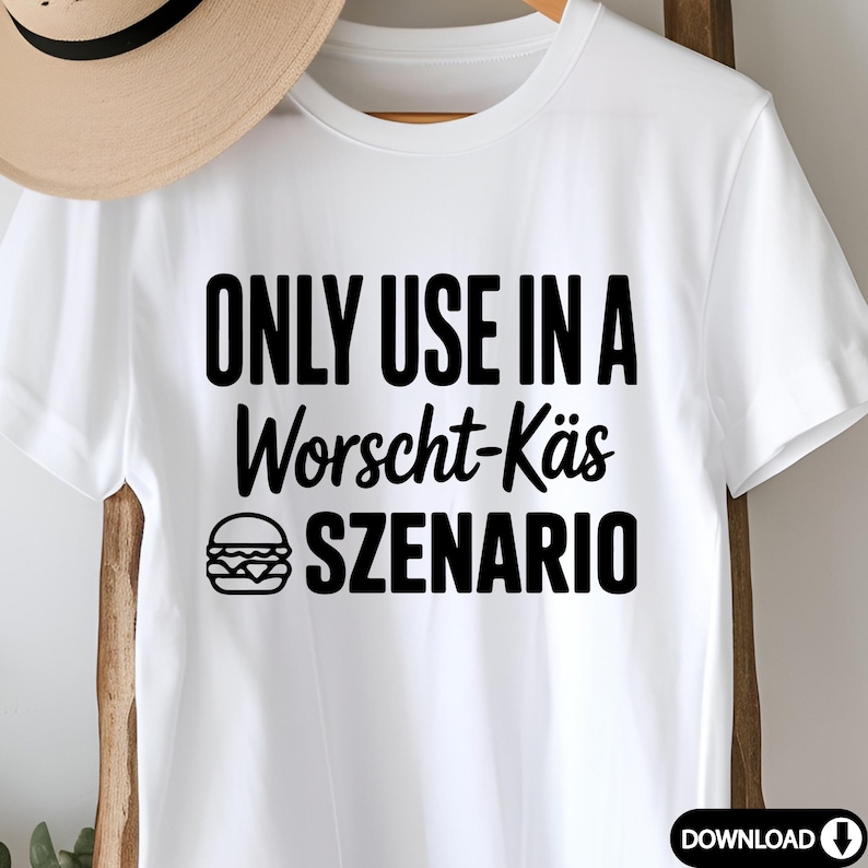 May include: White t-shirt with the text "ONLY USE IN A Worscht-K&auml;s SZENARIO" in black, along with a burger graphic. The shirt is hanging on a wooden rack. A straw hat is partially visible in the background.
