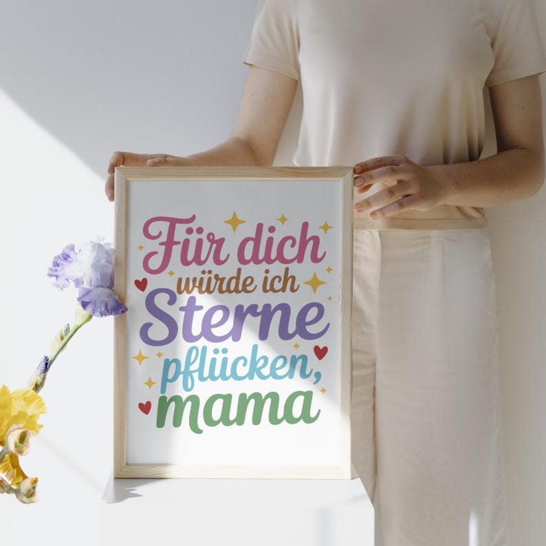 May include: A framed print with the German text "F&uuml;r dich w&uuml;rde ich Sterne pfl&uuml;cken, mama" in colorful script. The text is surrounded by stars and hearts. The frame is a light wood color.