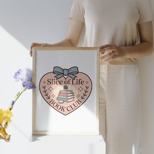 May include: A framed print featuring a heart-shaped design with the text "Slice of Life Book Club." The design includes a stack of books, a teacup, and a bow. The print is held by a person.
