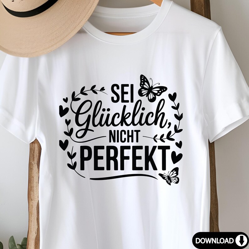 May include: White t-shirt featuring the German text "Sei Gl&uuml;cklich, Nicht Perfekt", translating to "Be Happy, Not Perfect". The design includes black butterflies and heart-shaped accents.