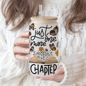Op de afbeelding: Een matglazen beker met een bamboe deksel en een doorzichtig rietje. De beker heeft de tekst "just one more chapter" met vlinder- en bloemenillustraties. Het ontwerp is in zwart, oranje en bruin.