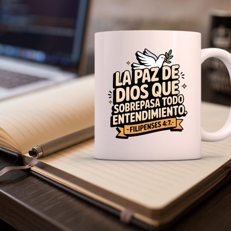 May include: White ceramic mug with a handle, featuring the text "LA PAZ DE DIOS QUE SOBREPASA TODO ENTENDIMIENTO" and "-FILIPENSES 4:7-". The design includes a white dove with an olive branch. The mug is on a notebook with a pen.