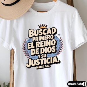 May include: White t-shirt with a colorful graphic design. The design features the text "Buscad Primero El Reino De Dios Y Su Justicia" in a stylized font, with a crown and laurel wreath. The text "Mateo 6:33" is also included.