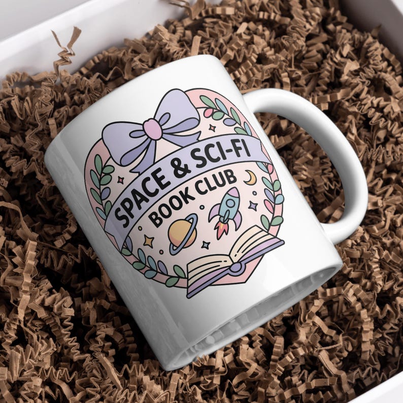 May include: White ceramic mug with a wraparound design featuring the text "SPACE & SCI-FI BOOK CLUB" in a banner, along with a rocket ship, planets, and an open book. The design is in pastel colors with a bow at the top.