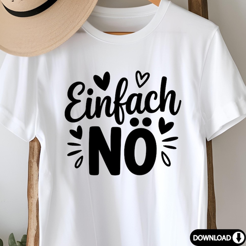 Puede incluir: Camiseta blanca con la frase alemana "Einfach N&ouml;" en negro, decorada con corazones y dise&ntilde;os de rayos de sol. Una camiseta casual de manga corta, perfecta para el uso diario. Un sombrero de paja es parcialmente visible en el fondo.