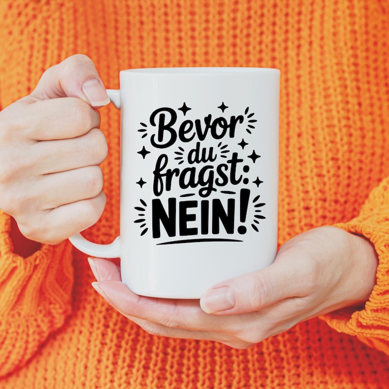 Puede incluir: Taza de cer&aacute;mica blanca con la frase alemana "Bevor du fragst: NEIN!" en escritura negra. La taza tiene un asa grande y la sostiene una persona con un su&eacute;ter naranja. El texto est&aacute; rodeado de estrellas decorativas.