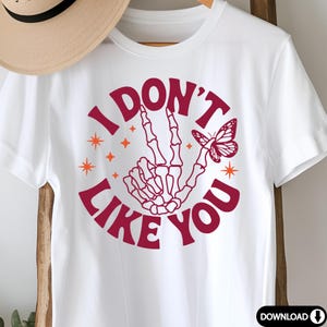 Peut inclure: T-shirt blanc avec un graphique circulaire rouge qui dit "Je n'aime pas toi" avec une main squelettique faisant un signe de paix et un papillon.