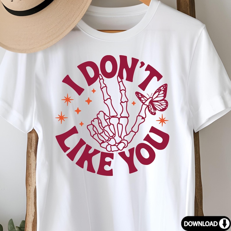 Peut inclure: T-shirt blanc avec un graphique circulaire rouge qui dit "Je n'aime pas toi" avec une main squelettique faisant un signe de paix et un papillon.