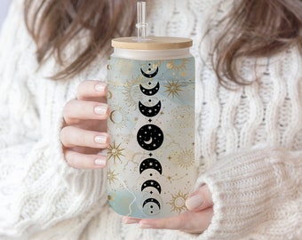 May include: A reusable glass tumbler with a bamboo lid and a straw. The tumbler features a celestial design with gold and white accents and a pattern of moons and stars.