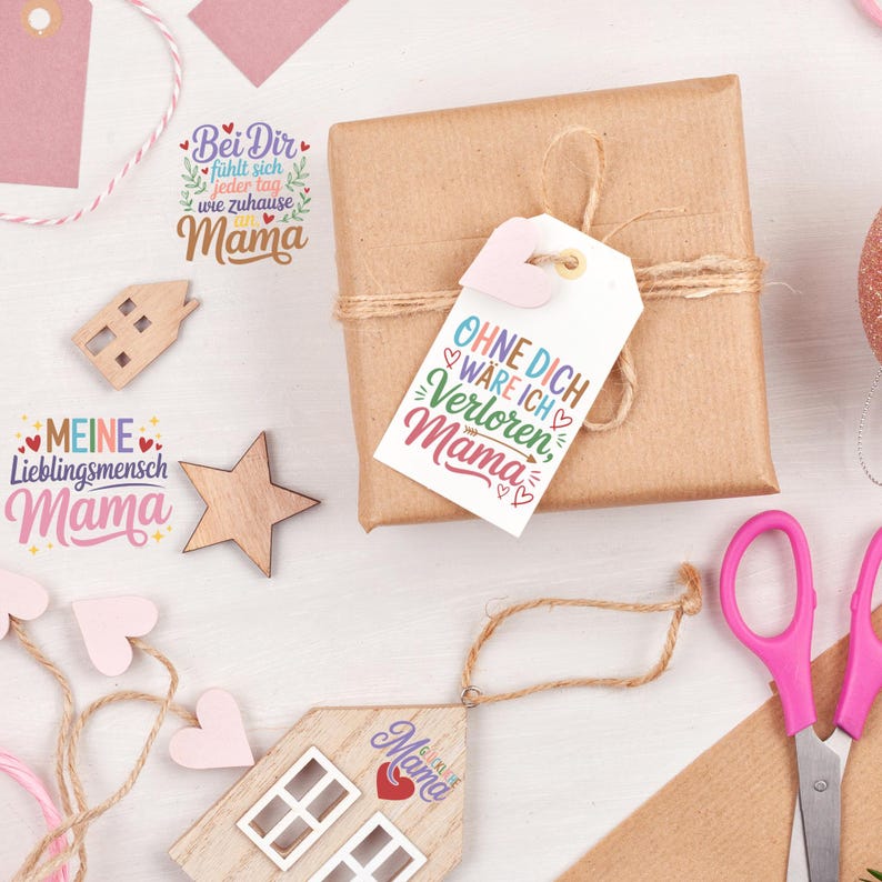May include: A wrapped brown gift box with a tag that reads "Ohne Dich w&auml;re ich verloren, Mama" in colorful script. Additional wooden decorations and tags with the word "Mama" are scattered around, suggesting a Mother's Day theme.