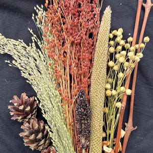 May include: A collection of dried floral elements, including wheat, red berries, and pinecones, arranged against a black background. The bouquet features a variety of textures and colors, with a focus on natural elements.