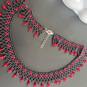 May include: A beaded necklace in black and red. The necklace has a repeating pattern of black beads with red accents and dangling red beads along the bottom edge. It has a silver-coloured clasp and is likely made of glass beads.