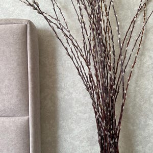 May include: A bouquet of pussy willow branches in a white ceramic vase with a textured surface. The branches are arranged in a vase on a black surface.