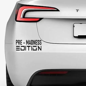 Puede incluir: Tesla Model 3 blanco con detalles negros y luces traseras. El coche tiene una pegatina negra en el parachoques trasero que dice "PRE-MADNESS EDITION".