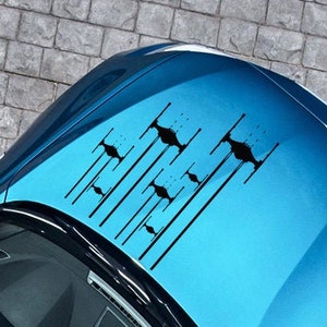 May include: A blue car with a black Star Wars X-Wing fighter decal on the hood.