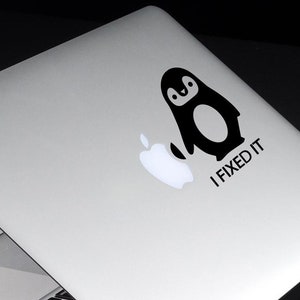 Peut inclure: Un ordinateur portable argenté avec un autocollant de pingouin noir sur le couvercle. L'autocollant dit "J'ai réparé".