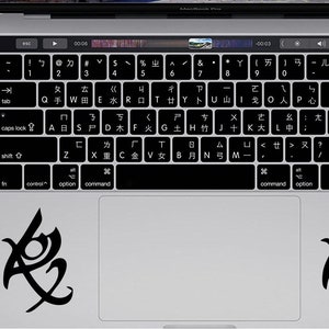 May include: A silver laptop computer with a black keyboard and a black trackpad. The trackpad has two black stickers on it, each with a stylized symbol.
