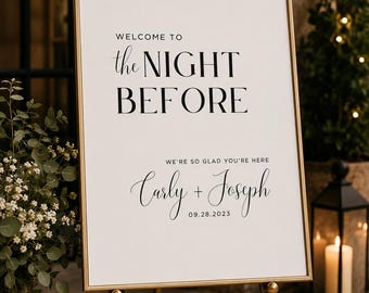 May include: A gold-framed sign on a gold easel. The sign reads "WELCOME TO the NIGHT BEFORE" in black text. Below, it says "WE'RE SO GLAD YOU'RE HERE" and the names "Carly + Joseph" with the date "09.28.2023".