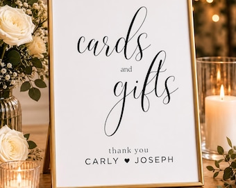 May include: A framed sign with gold trim, displaying the words "cards and gifts" in elegant script. Below, it reads "thank you Carly ♥ Joseph." The sign is set on a wooden surface, with flowers and candles in the background.