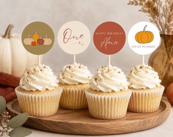 May include: Four cupcakes with white frosting and sprinkles, each topped with a circular paper topper on a wooden stick. The toppers feature autumn-themed designs including pumpkins, the text One, Happy Birthday Alexa, and Little Pumpkin.