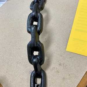 Pode incluir: Puxador de porta de corrente de metal preto. O puxador é feito de uma série de elos conectados, cada um com uma forma arredondada. O puxador é projetado para ser montado em uma porta.