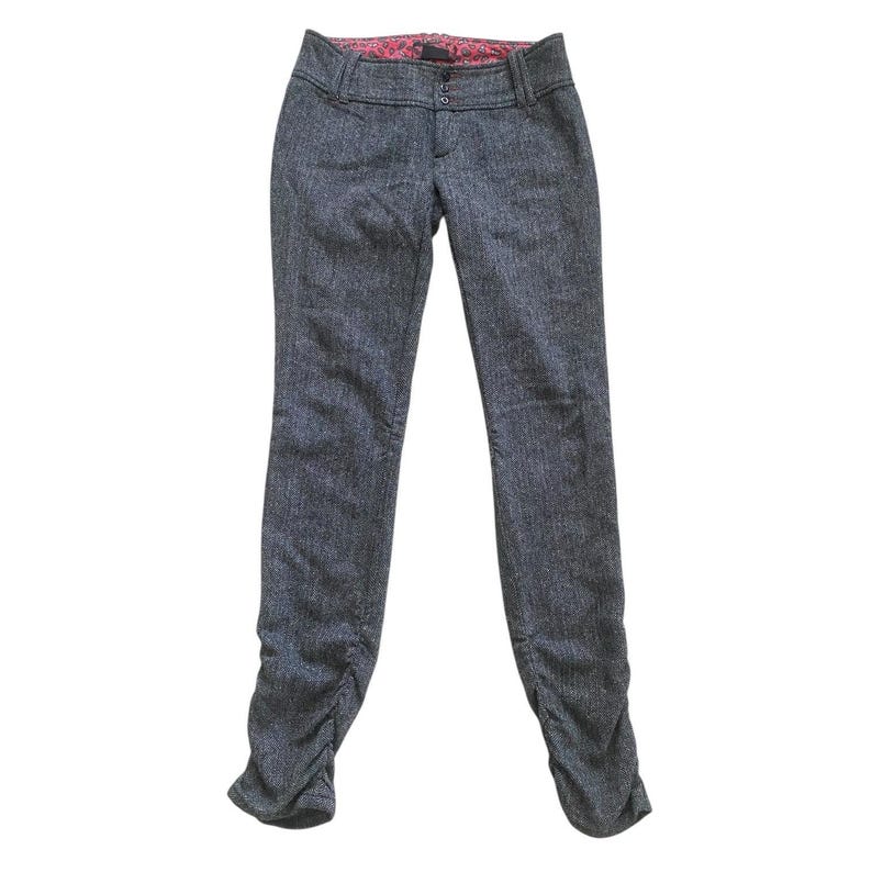 Op de afbeelding: Grijze tweed broek met een getailleerde snit. De broek heeft een knoop- en ritssluiting, riemlussen en een roze voering met patroon. De pijpen hebben een gerimpeld detail bij de enkels.