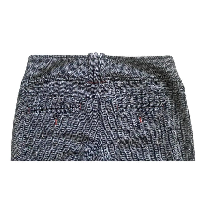 Op de afbeelding: Close-up van de achterkant van een grijze broek met visgraatpatroon. De broek heeft twee achterzakken met rode stiksels en een detail van een riemlus. De stof heeft een getextureerde uitstraling.