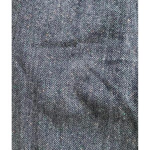 Op de afbeelding: Close-up van een textiel met een visgraatpatroon. De stof is voornamelijk donkerblauw met witte en kleine groene en bruine vlekken. De weving cre&euml;ert een subtiel, diagonaal gestreept effect.