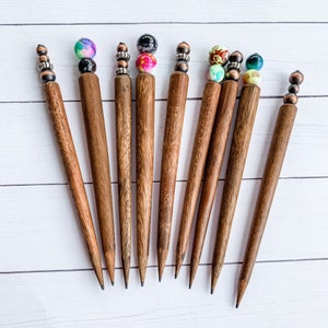 May include: Ten wooden hair sticks with colorful beads at the top. The sticks are brown and have a smooth finish.