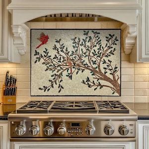 May include: A kitchen backsplash mosaic depicting a tree with green leaves and two red cardinal birds. The mosaic is above a stainless steel gas range. The kitchen features white cabinetry.