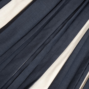 May include: Diagonal view of a fabric with alternating navy blue and off-white stripes. The fabric appears to be pleated or folded, creating a textured surface with shadows and highlights.