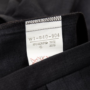 May include: Close-up of a black garment with a white tag attached. The tag displays the text "WI-S40-904" and Japanese characters indicating the fabric composition: 70% polyester and 30% wool. The garment's fabric appears to be a dark, solid color.