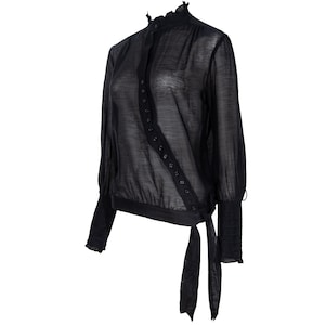 May include: Black long-sleeved blouse with a high ruffled collar and button closure. The sheer fabric drapes loosely, with a tie at the waist and fitted cuffs. A stylish top for various occasions.