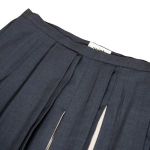 May include: Close-up of a pair of navy blue pleated skirt with a split front. The skirt has a tailored look with a visible waistband and a small white tag with the word "twist" on it.