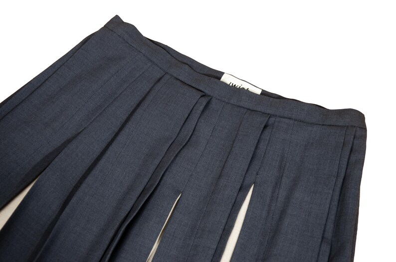 May include: Close-up of a pair of navy blue pleated skirt with a split front. The skirt has a tailored look with a visible waistband and a small white tag with the word "twist" on it.