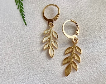 May include: A pair of gold leaf dangle earrings with a hoop closure. The earrings feature a delicate leaf design.