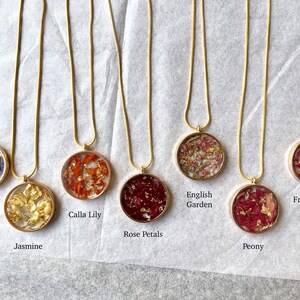 May include: Ten gold necklaces with round glass pendants containing pressed flowers. The pendants feature different flower varieties, including lavender, jasmine, calla lily, rose petals, English garden, peony, and French lilac.