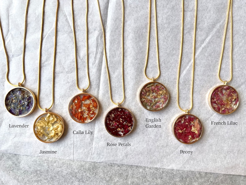 May include: Ten gold necklaces with round glass pendants containing pressed flowers. The pendants feature different flower varieties, including lavender, jasmine, calla lily, rose petals, English garden, peony, and French lilac.