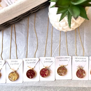 May include: Eight gold chain necklaces with round pendants featuring pressed flowers and gold flakes. Each pendant is labeled with a flower name and a short description, such as "Lavender, Calm and Elegant" or "Rose Petals, Passionate and Bold".