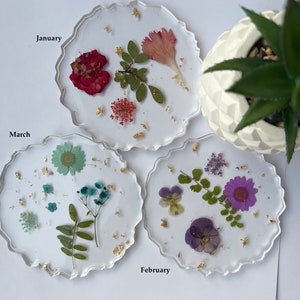 May include: Three round resin coasters with pressed flowers and gold leaf. The coasters are labeled "January", "February", and "March".