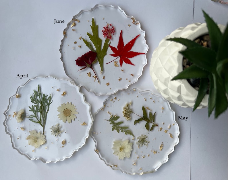May include: Three clear resin coasters with pressed flowers and gold leaf. The coasters are labeled "April", "May", and "June".