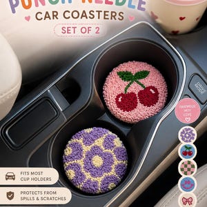 May include: Punch needle car coasters, set of 2, in a car cup holder. One coaster features a cherry design on a pink background, the other a purple floral pattern. Text reads "Fits Most Cup Holders" and "Protects From Spills & Scratches."